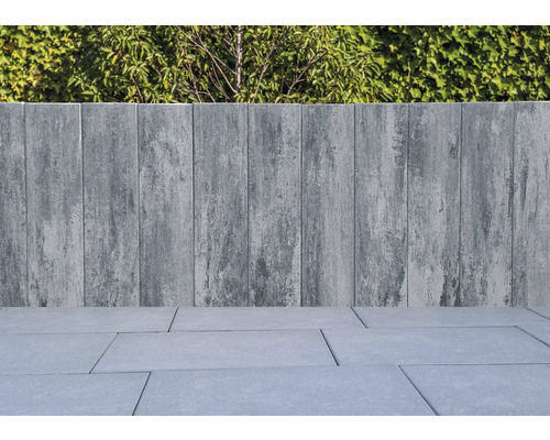 Graue Steinmauer und Bodenplatten mit Grünpflanzen im Hintergrund.