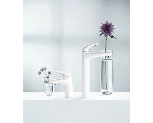 Zwei weiße Waschtischarmaturen unterschiedlicher Höhe neben Blumengestecken in Vasen