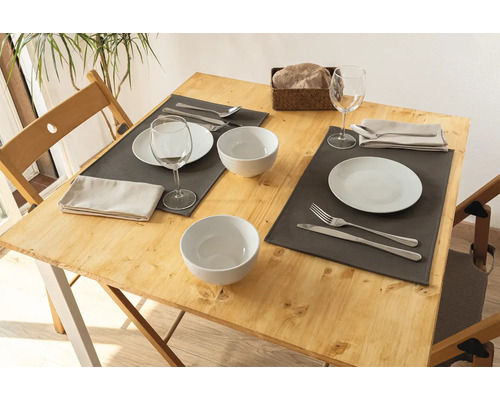 Gedeckter Holztisch mit Geschirr, Besteck und grauen Tischsets.