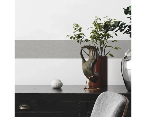 Dekorative Accessoires auf einer schwarzen Kommode vor einer Wand mit grauen und weißen Streifen