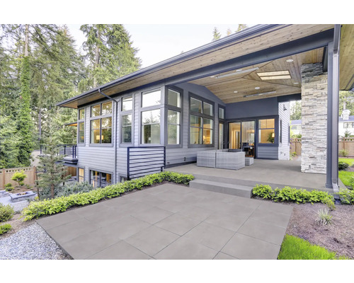 Terrasse mit grauen Fliesen vor einem modernen Haus mit großem Fensterbereich.