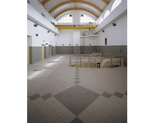 Innenansicht eines großen Raumes mit Fliesenboden, Kran und Fenstern