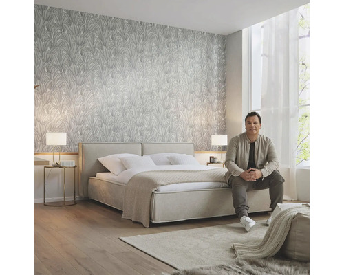 Helles Schlafzimmer mit gemusterter Tapete, Doppelbett, Teppich und sitzendem Mann