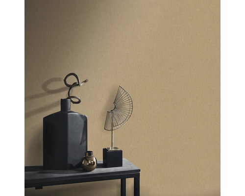 Dekorative Szene mit einer strukturierten Tapete, ergänzt durch eine schwarze Vase, eine goldene Kugel und eine fächerförmige Metallskulptur auf einem Tisch.