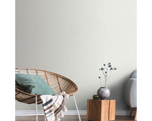 Heller Wohnraum mit Rattan-Sessel, Holztisch und dezent gemusterter Tapete.