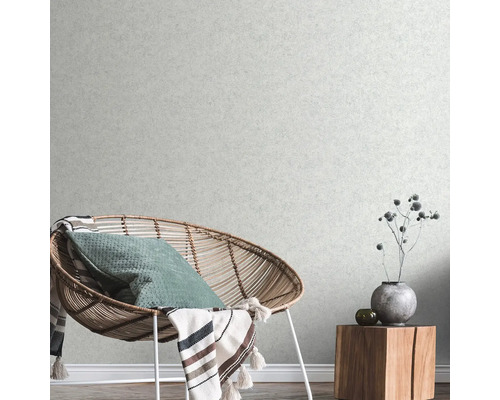 Wohnzimmer mit Rattansessel, Kissen, Decke und Holzbeistelltisch mit Dekoration vor einer strukturierten Tapete