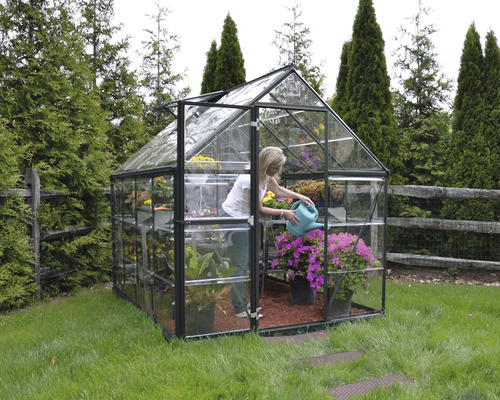 Gewächshaus mit Pflanzen und einer Frau, die mit einer Gießkanne gießt