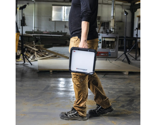 Eine Person trägt eine Scangrip Arbeitsleuchte in einer Werkstatt.