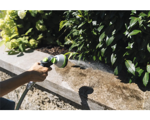 Gartenszene mit einer Person, die eine Gartenbrause zur Reinigung einer Mauer verwendet.