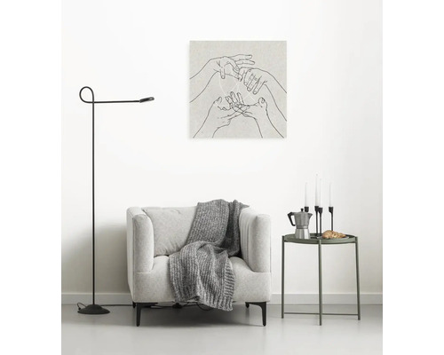 Wohnzimmer-Szene mit Sessel, Stehlampe, Beistelltisch und Wandbild mit Händen