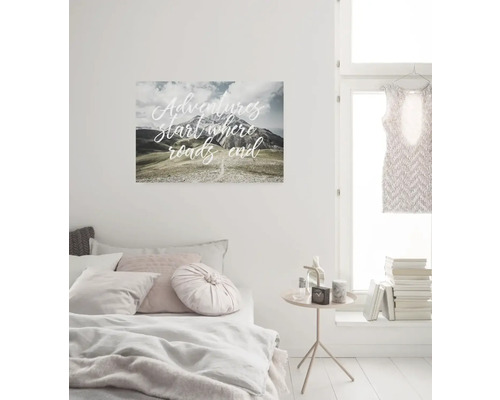 Schlafzimmer mit Bett, Beistelltisch und Wandbild mit Bergmotiv und dem Schriftzug Abenteuer beginnen, wo die Straßen enden.