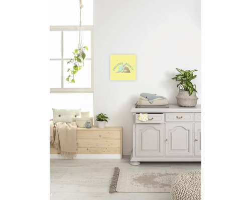 Szene eines hellen Raumes mit Kommode, Holzkiste, Teppich und gerahmtem Bild mit der Aufschrift Precious Bounty an der Wand