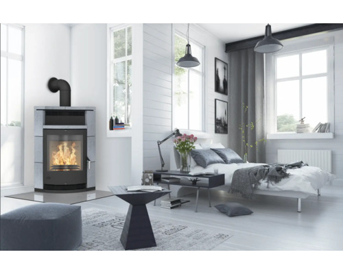 Helles Schlafzimmer mit Kaminofen, Bett und Fenstern für eine freundliche Atmosphäre.