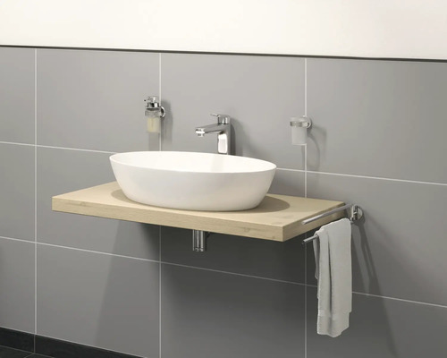 Waschbecken auf Holzplatte mit Armatur, Seifenspender, Zahnputzbecher und Handtuchhalter vor grauer Wand