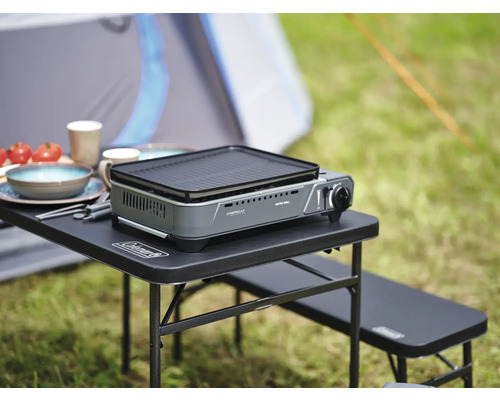 Campingtisch mit Gaskocher, Geschirr und Lebensmitteln im Freien