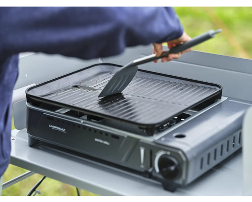 Campingtischgrill mit Grillplatte und Person mit einem Spatel