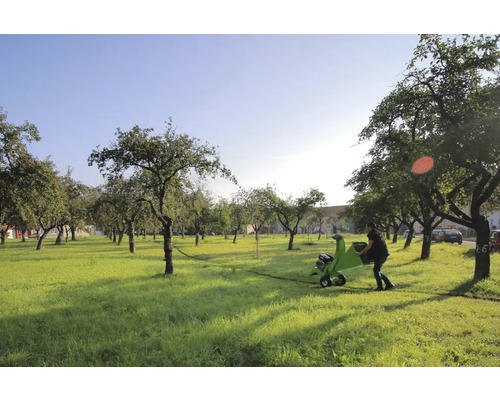 Eine Person schiebt einen Häcksler durch einen Garten mit Bäumen.