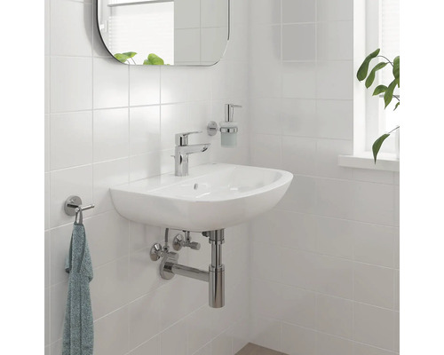 Badezimmerwaschbecken mit Armatur, Spiegel, Seifenspender und Handtuchhalter an einer gefliesten Wand.