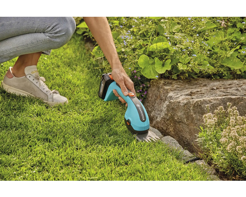 Person schneidet Rasen mit einer Akku-Grasschere von Gardena entlang eines Steins.
