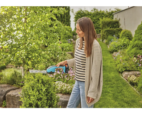 Eine Frau schneidet eine Hecke mit einer Akku-Heckenschere in einem Garten.