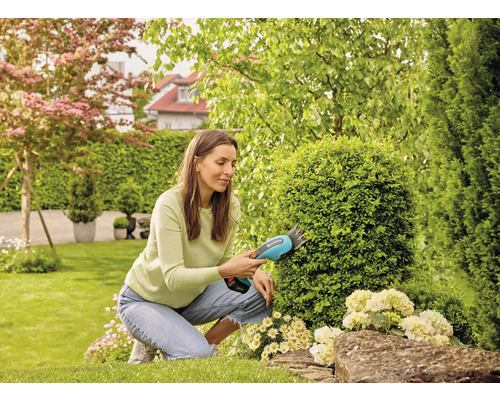 Frau schneidet Büsche mit Akku-Strauchschere im Garten.
