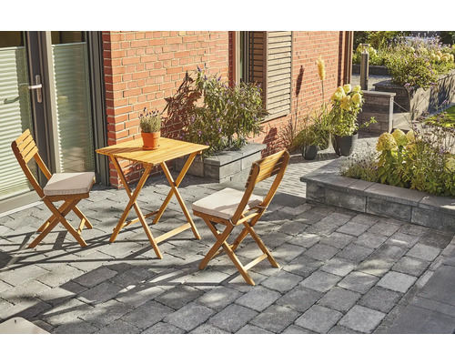 Gartenszene mit Holztisch und zwei Stühlen auf Pflastersteinen vor einem Haus