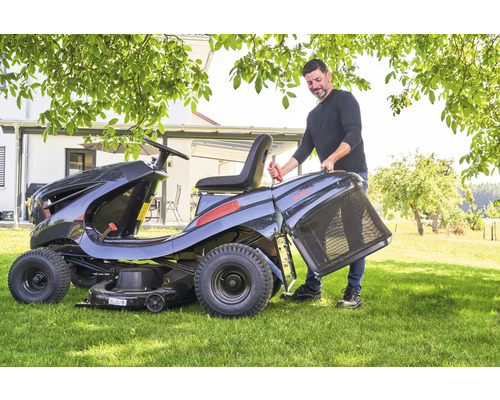 Mann befestigt Fangkorb an einem Aufsitzmäher im Garten.