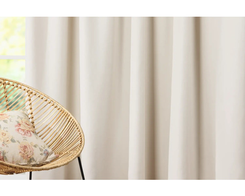 Gardine und Korbsessel mit Kissen vor einem Fenster