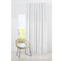 Innenaufnahme eines Wohnraums mit weißem Vorhang, Rattansessel und floralem Kissen vor einem Fenster