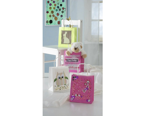 Dekorierte Geschenktüten in verschiedenen Designs mit einem Teddybär auf einem weißen Stuhl.