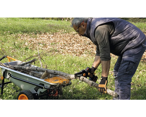 Mann sägt mit einer Akku-Kettensäge einen Ast vor einer Schubkarre.