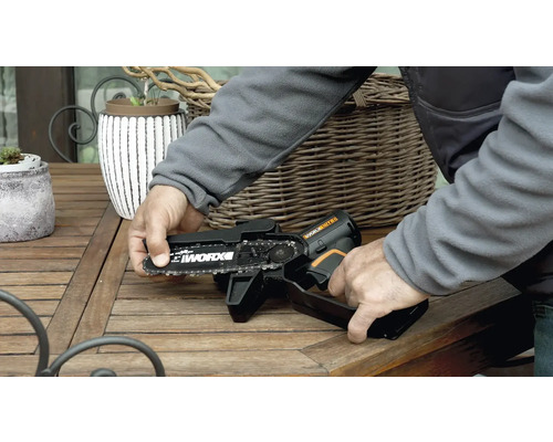 Eine Person bedient eine Akku-Kettensäge der Marke Worx auf einem Holztisch