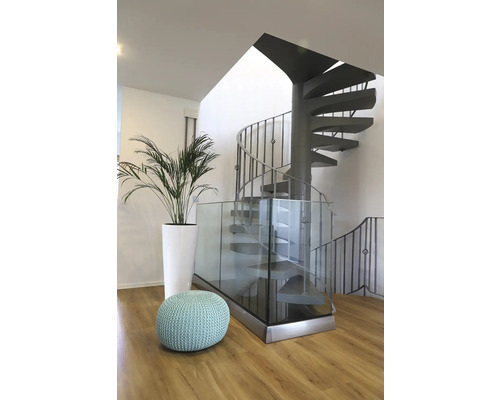 Innenaufnahme mit Wendeltreppe, Glasgeländer, Pflanze im Topf und Sitzpouf in einem hellen Raum.