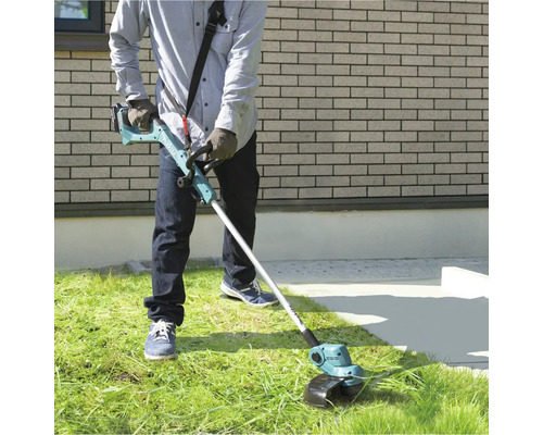 Eine Person benutzt einen Akku-Rasentrimmer im Garten, um Gras zu schneiden.