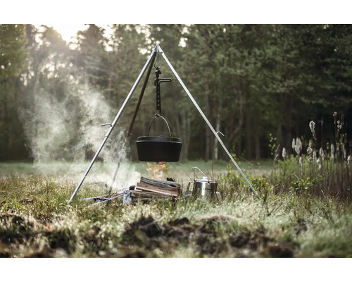 Gusseisenkessel hängt über einem Lagerfeuer an einem Dreibein im Freien.