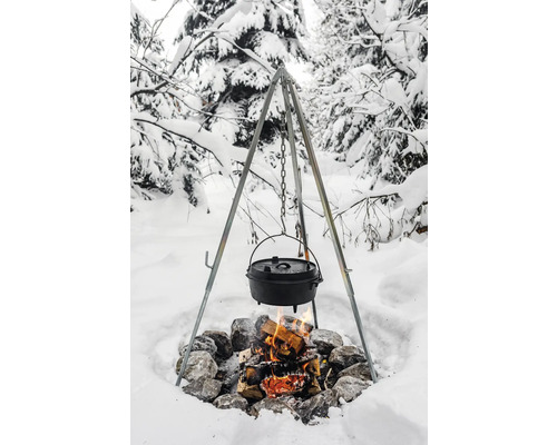Dreibein über Lagerfeuer mit gusseisernem Topf in verschneiter Landschaft