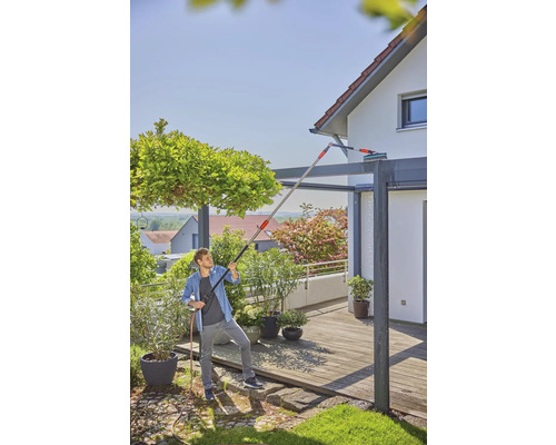 Mann reinigt mit einer Teleskopstange und Wasserschlauch ein Terrassendach.