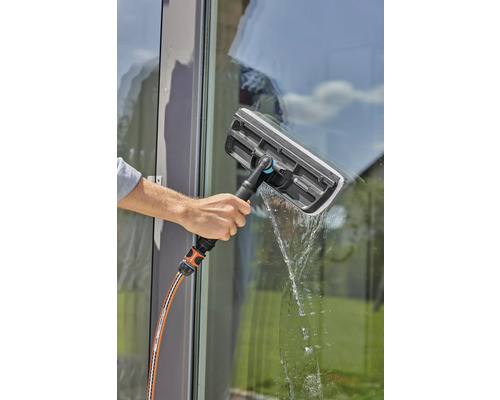 Eine Person reinigt ein Fenster mit einem Fensterwischer und einem Wasserschlauch.