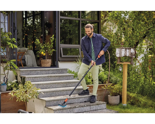 Mann reinigt Außentreppe mit Bürste und Wasseranschluss