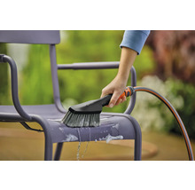 Eine Person reinigt einen Gartenstuhl mit einer Bürste und einem Wasserschlauch.