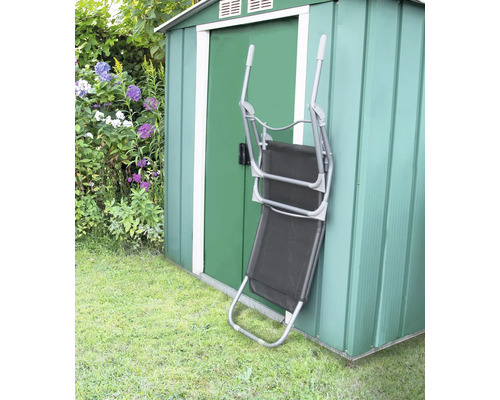 Klappbarer Liegestuhl aus Metall und Textil steht an einem grünen Geräteschuppen im Garten.