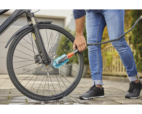 Person reinigt ein Fahrrad mit einer Bürste und einem Wasserschlauch.