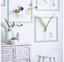 Dekorative Wandgestaltung mit Blumen in Vasen, die in Rahmen an einer Wand hängen, und einem Sideboard mit Pflanzen.
