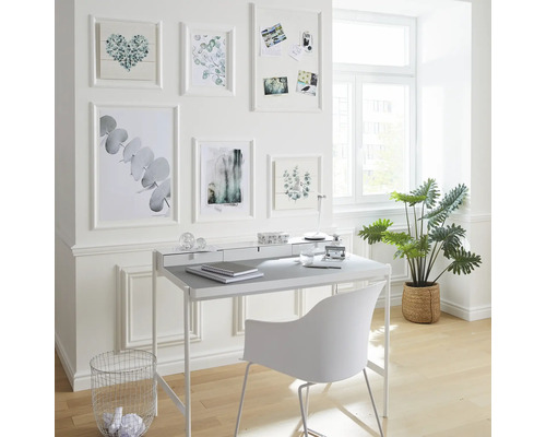 Helles Arbeitszimmer mit Schreibtisch, Stuhl, Zimmerpflanze und Bilderrahmen an der Wand