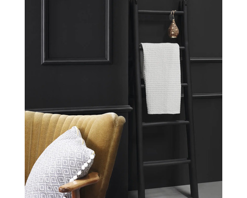 Dekorative Leiter mit Handtuch, Sessel und Kissen vor dunkler Wand