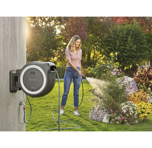 Frau bewässert Blumen mit einer an der Wand montierten Schlauchtrommel im Garten.