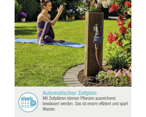 Gartenbewässerungssystem mit Bewässerungscomputer und Wasserhahn an Holzpfosten in einem Garten.