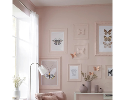 Wohnzimmer mit Bilderrahmen und Schmetterlingsmotiven an der Wand, Stehlampe und dekorativen Vasen auf dem Tisch.