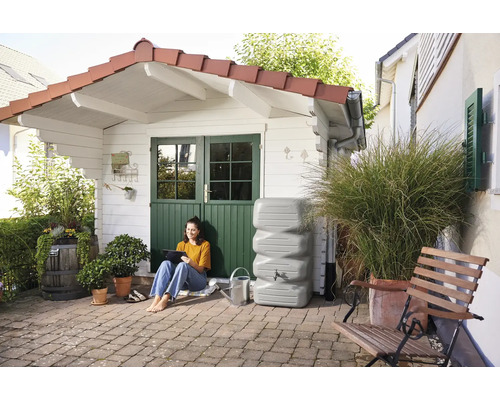 Gartenansicht mit Zisterne, Frau mit Tablet und Gartenhaus