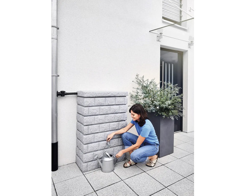 Frau befüllt Gießkanne an einem Regenwassertank im Garten.